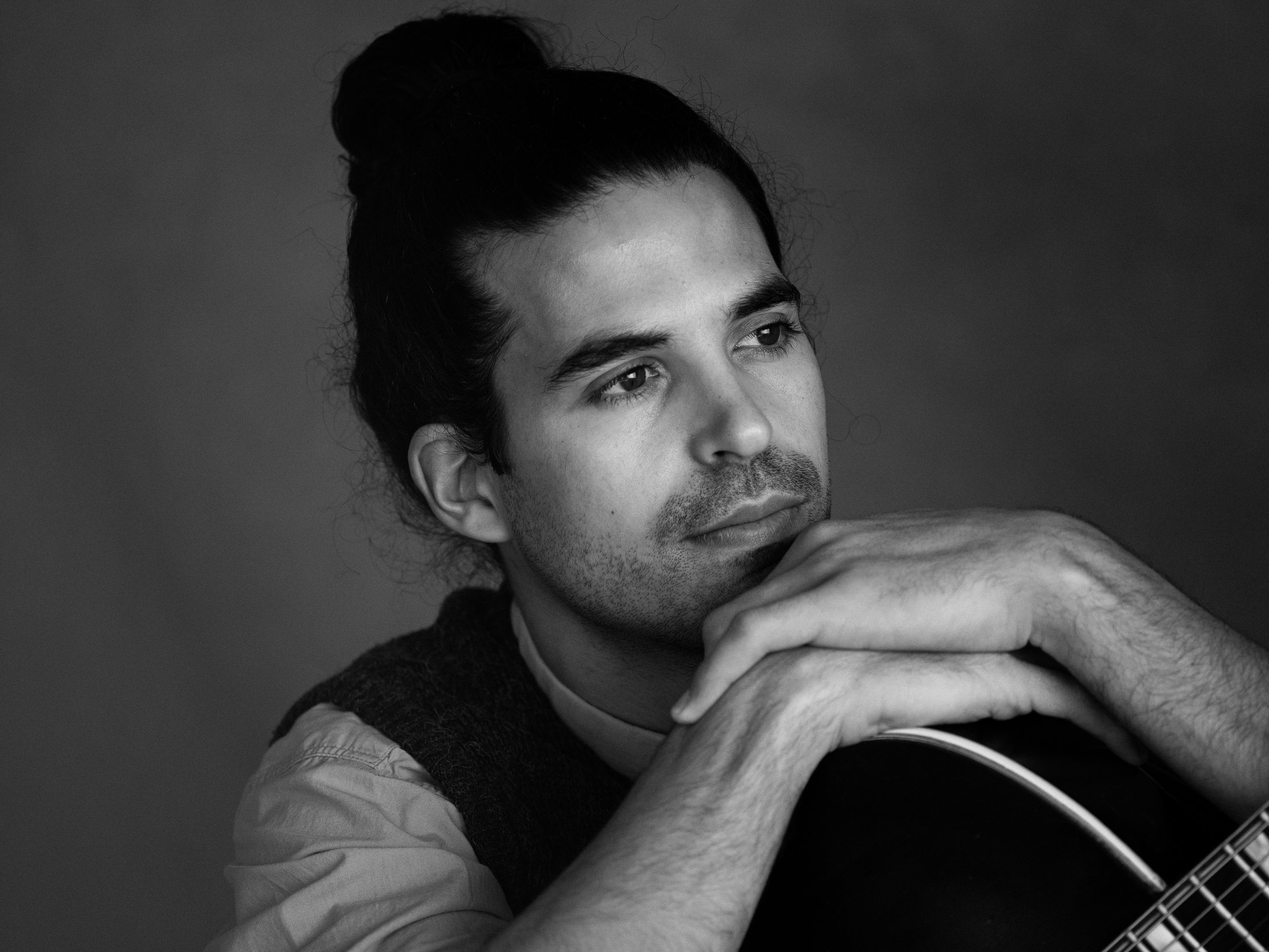 Close portrait of Kai Gluska, chin resting on hand, holding guitar