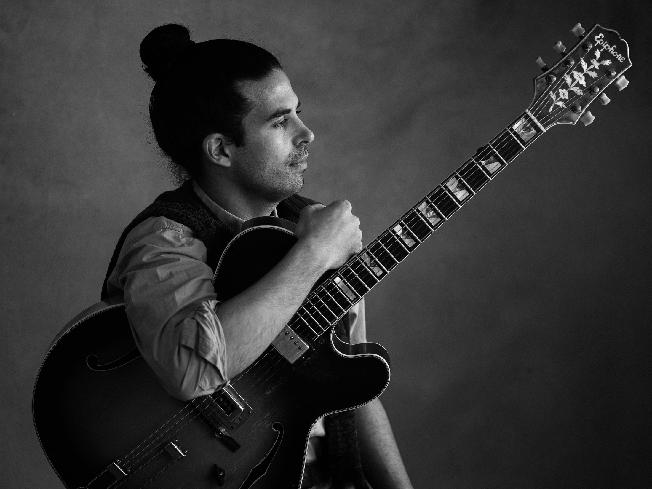 Kai Gluska holding an archtop guitar, in profile